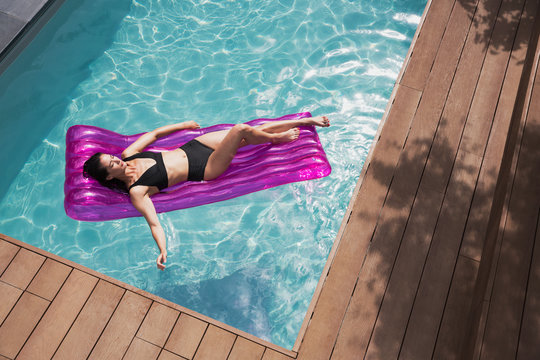 Serene woman relaxing on inflatable raft in sunny summer swimming pool