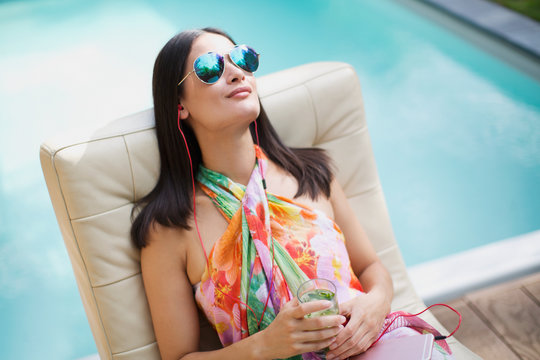 Serene woman with sunglasses and headphones relaxing, listening to music at summer poolside