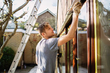 Male painter painting home exterior window trim