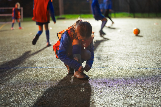 Girl soccer player tying shoe on field at night