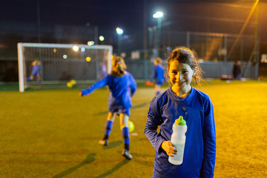 Portrait smiling girl soccer player drinking water on field at night