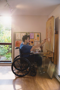 Male artist in wheelchair painting in art studio