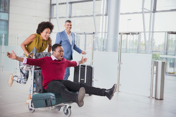 Playful couple running with luggage cart in airport