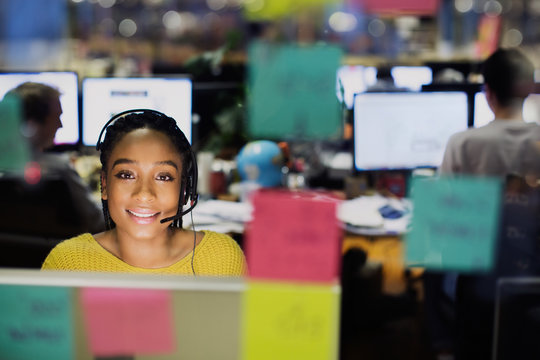 Portrait confident, smiling businesswoman with headset working at computer behind adhesive notes in office
