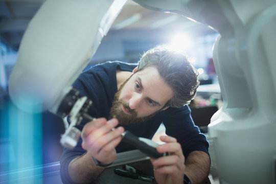Focused male engineer with screwdriver fixing robotic arm