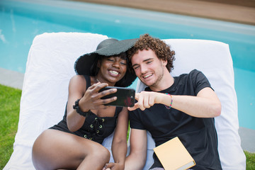 Happy young couple taking selfie with camera phone at poolside