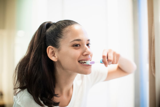 Happy woman brushing teeth in bathroom mirror