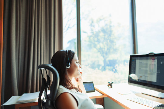 Businesswoman with headset working at computer in sunny home office