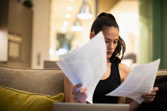 Woman reading paperwork at laptop on sofa