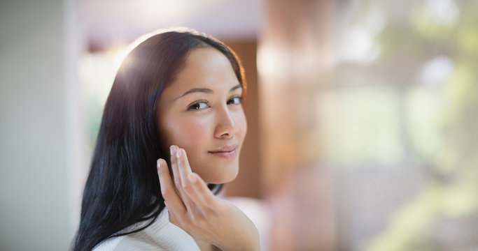 Portrait confident young woman applying moisturizer to face