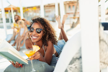 Portrait happy, carefree young woman reading book and drinking cocktail on beach