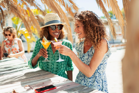 Happy young women friends drinking cocktails on sunny beach bar