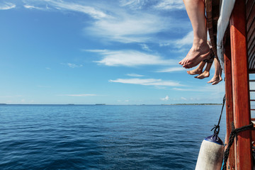 Bare feet dangling over sunny ocean dock, Maldives