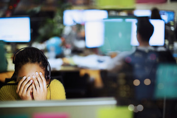 Tired, stressed businesswoman with head in hands at computer in office