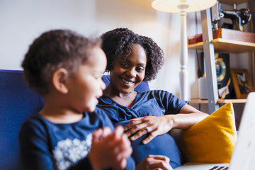 Happy pregnant mother and daughter using laptop on sofa