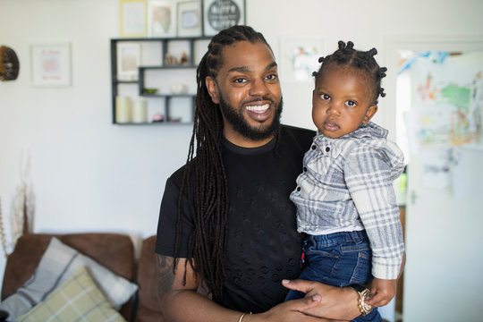 Portrait happy father with long braids holding toddler son