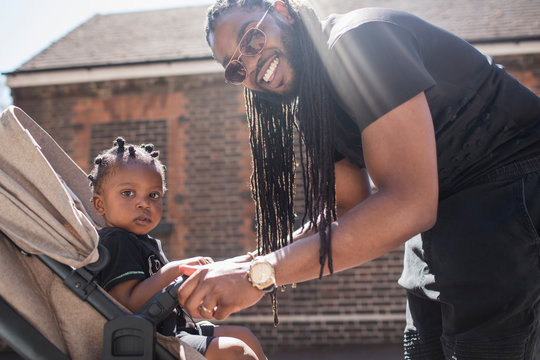 Portrait happy father with long braids fastening toddler son in stroller