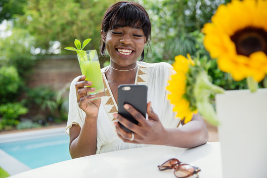 Happy young woman drinking cocktail and video chatting at poolside
