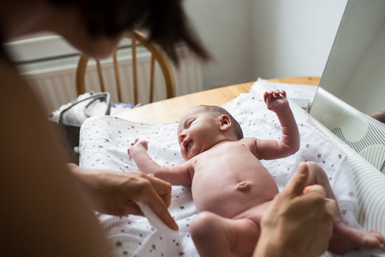 Mother changing diaper of newborn baby son on changing table