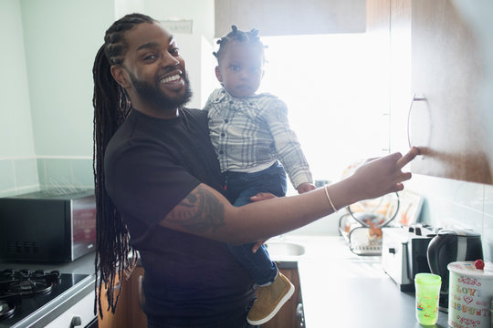 Portrait happy father holding toddler son in apartment kitchen