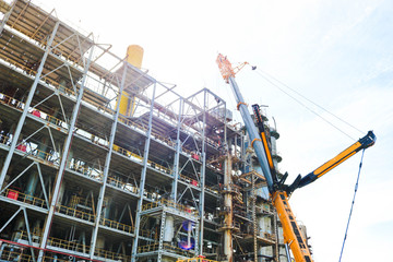 Construction and installation work with a powerful construction crane of a large new industrial oil refining petrochemical chemical plant with pipes, columns, railings, stairs and equipment