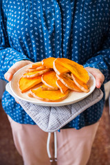 Woman hands holds baked squash,  roasted or grilled pumpkin slices on a plate.