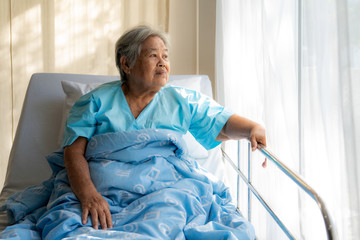 Asian depressed elderly woman patients lying on bed looking out the window in hospital. Elderly...