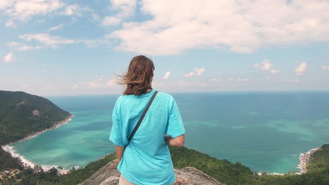 4k Dolly shot. A young woman standing at the edge of the rock with a sea view. The Gulf of Thailand, Koh Phangan Island, Thailand.