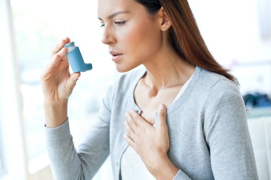 Young woman using inhaler touching chest