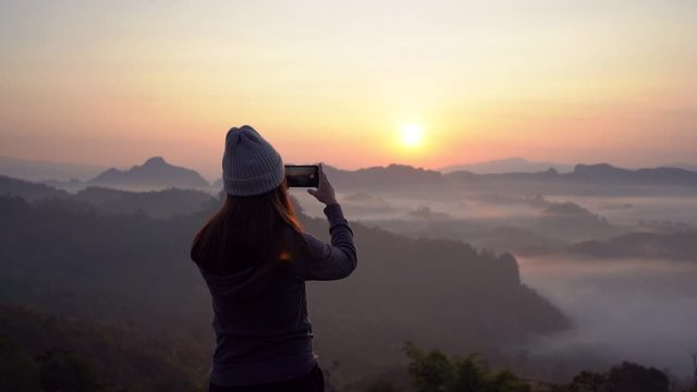 Young woman traveler taking photo with smart phone at sea of mist and sunset over the mountain at Mae Hong Son, Thailand