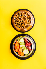 Healthy feed for cats and dogs. Bowls full of dry feed, meat and vegetables on yellow background top-down