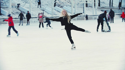 A young blonde woman professional figure skater skating on the outdoors ice rink around people © KONSTANTIN SHISHKIN