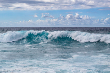 Waves crashing over in the blue ocean with white clouds in the blue sky