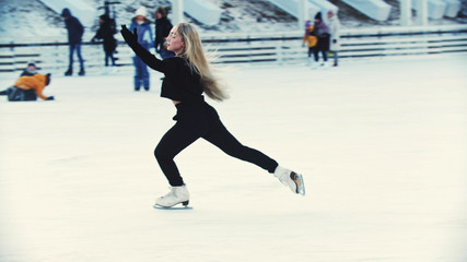 A young blonde attractive woman figure skater skating on the outdoors ice rink around people © KONSTANTIN SHISHKIN
