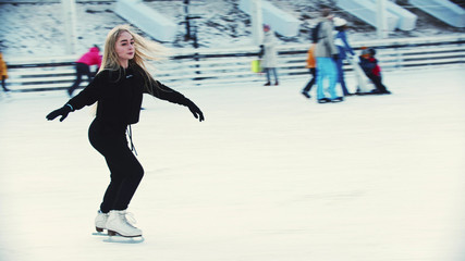 A young woman figure skater skating on the ice rink around people