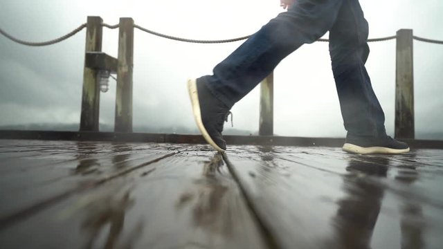 Man wearing jeans and tennis shoes walking along a wet dock on a rainy day in the Pacific Northwest.
