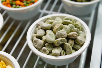 Frozen beans lies in a white cup. Next to the plates are other frozen vegetables and fruits.
