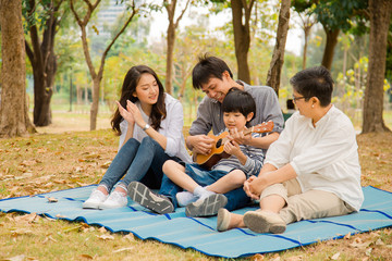 Happy Asian family having fun and enjoying picnic party with playing Ukulele in park,Family...