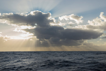 Obraz premium Sunbeams or light rays in a cloudy sky over the ocean.