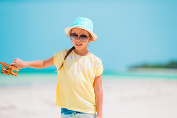 Happy little girl with toy airplane in hands on white sandy beach.