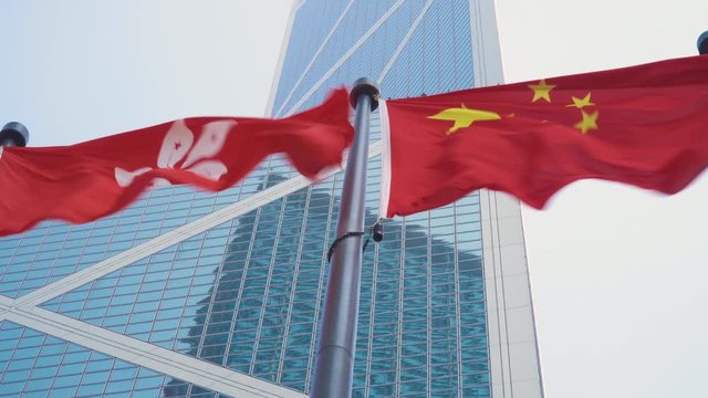 Hong Kong Flag Waving Next to China Flag in a Downtown Financial District Against Modern Bank Office Building