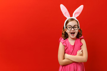 Happy easter. Funny cheerful little girl in rabbit ears and glasses on a red background. The child...