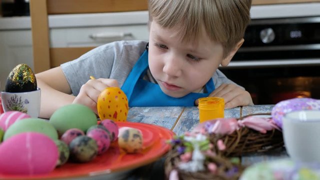 Five years old child boy kid coloring easter eggs in the kitchen.