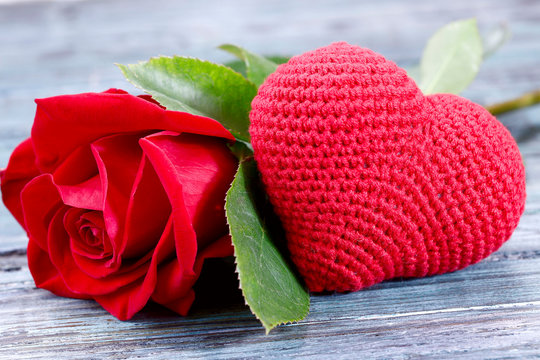 Valentine's day background. On a gray wooden background in the center is a red knitted heart and a red rose. Close-up, horizontal, side view, free space for text.