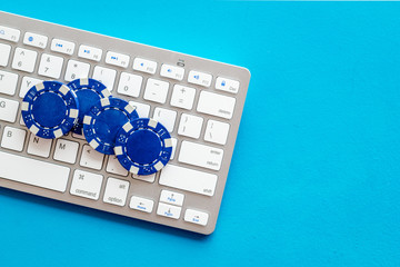 Online poker. Chips near keyboard on blue background top-down copy space