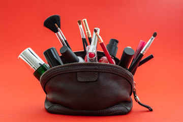 Make-up bag with cosmetics and makeup accessories against red background