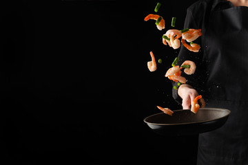 Banner with sea food. The chef cooks shrimps with green beans, freezing in motion. On a black background. Healthy eating.