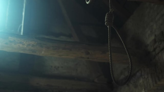 Rope noose hangs ominously from beam in dark barn, low angle