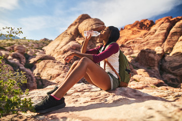 Naklejka premium female hiker drinking from water bottle on cliff ledge at red rock canyon