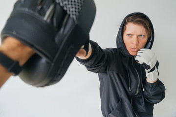 Fighter woman training with trainer. A woman in gloves and a black hoodie hits the trainer's gloves.